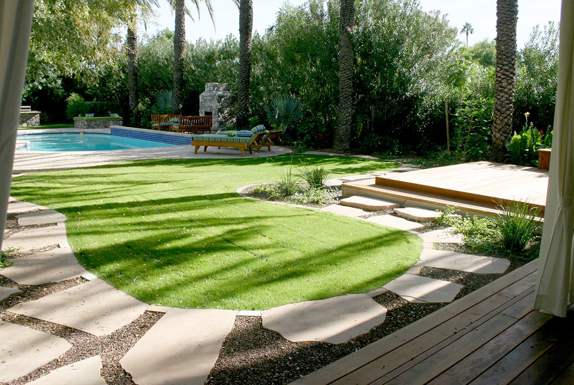Tropical inspired landscape design by On Site Landscape in Paradise Valley, Arizona featuring a sparkling pool, covered patio, outdoor fireplace as well as lush plantings and a green lawn, perfect for family and friends spending time outside.