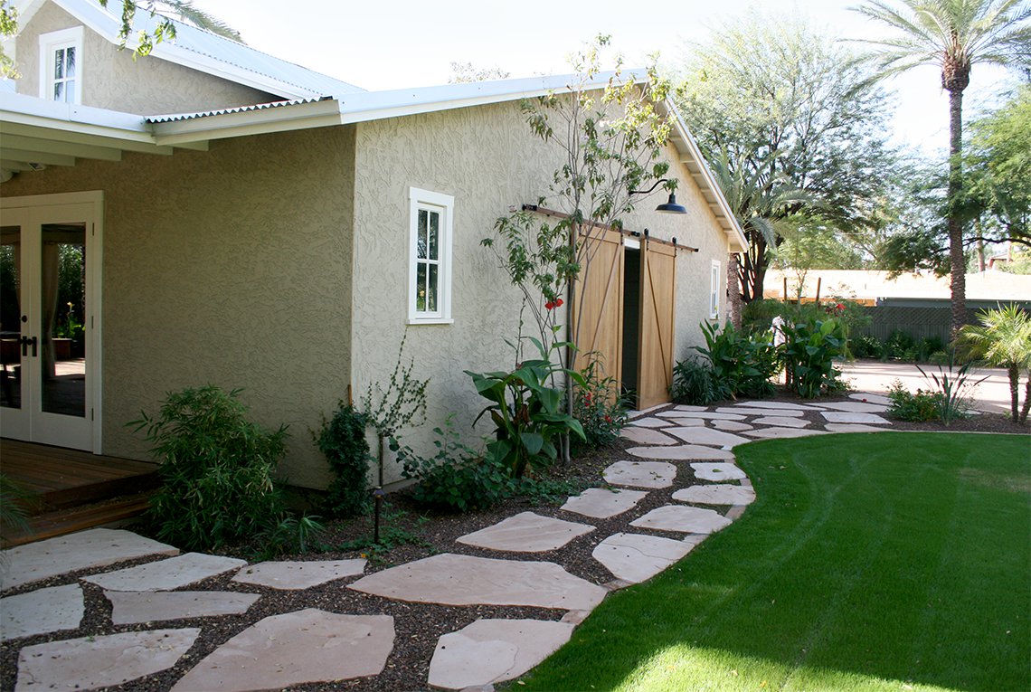 Pathway, lawn and patio details leading to the tropical inspired landscape design by On Site Landscape in Paradise Valley, Arizona featuring a sparkling pool, covered patio, outdoor fireplace as well as lush plantings and a green lawn, perfect for family and friends spending time outside.