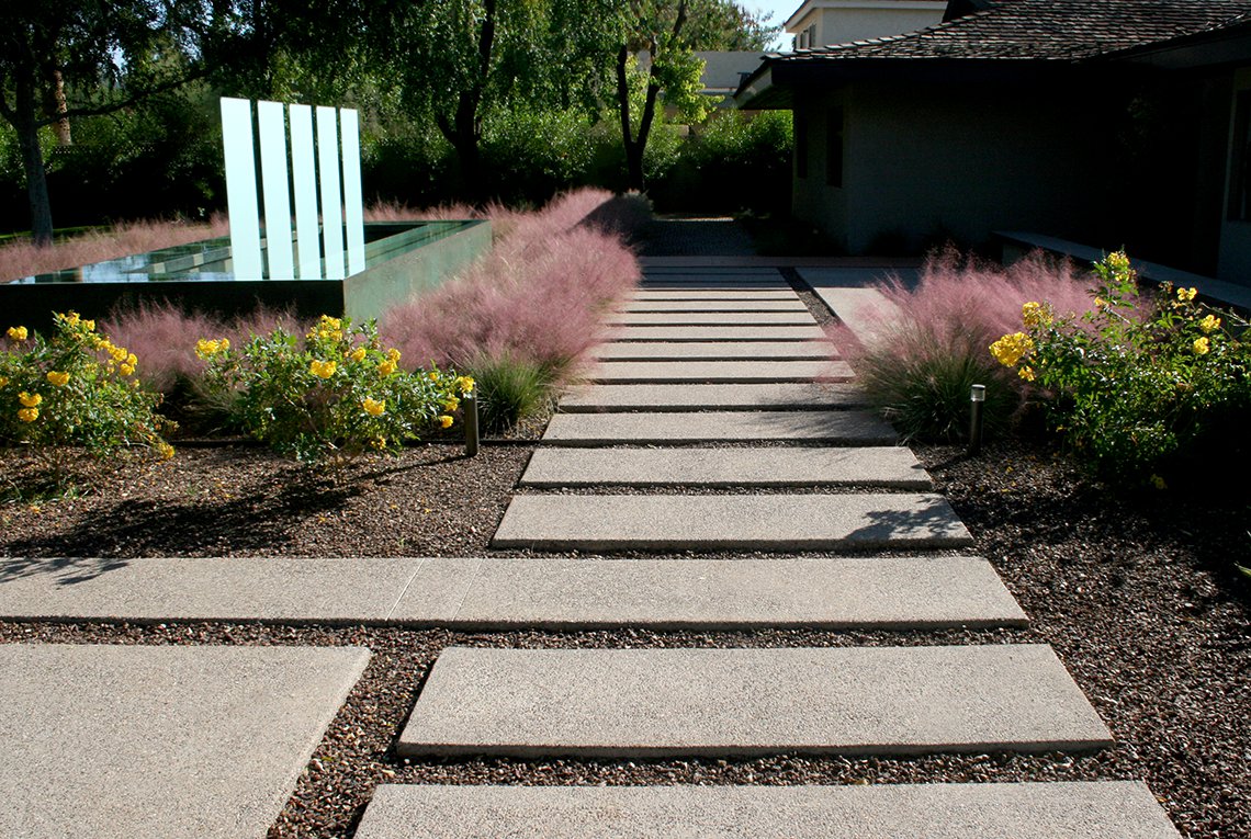 Custom contemporary landscape design by On Site Landscape in Arcadia, Arizona features a modern water feature with glass panels that echo the rectangular grid of hardscape steppers as well as the organic grid plantings of flowering shrubs and feathery desert grasses.